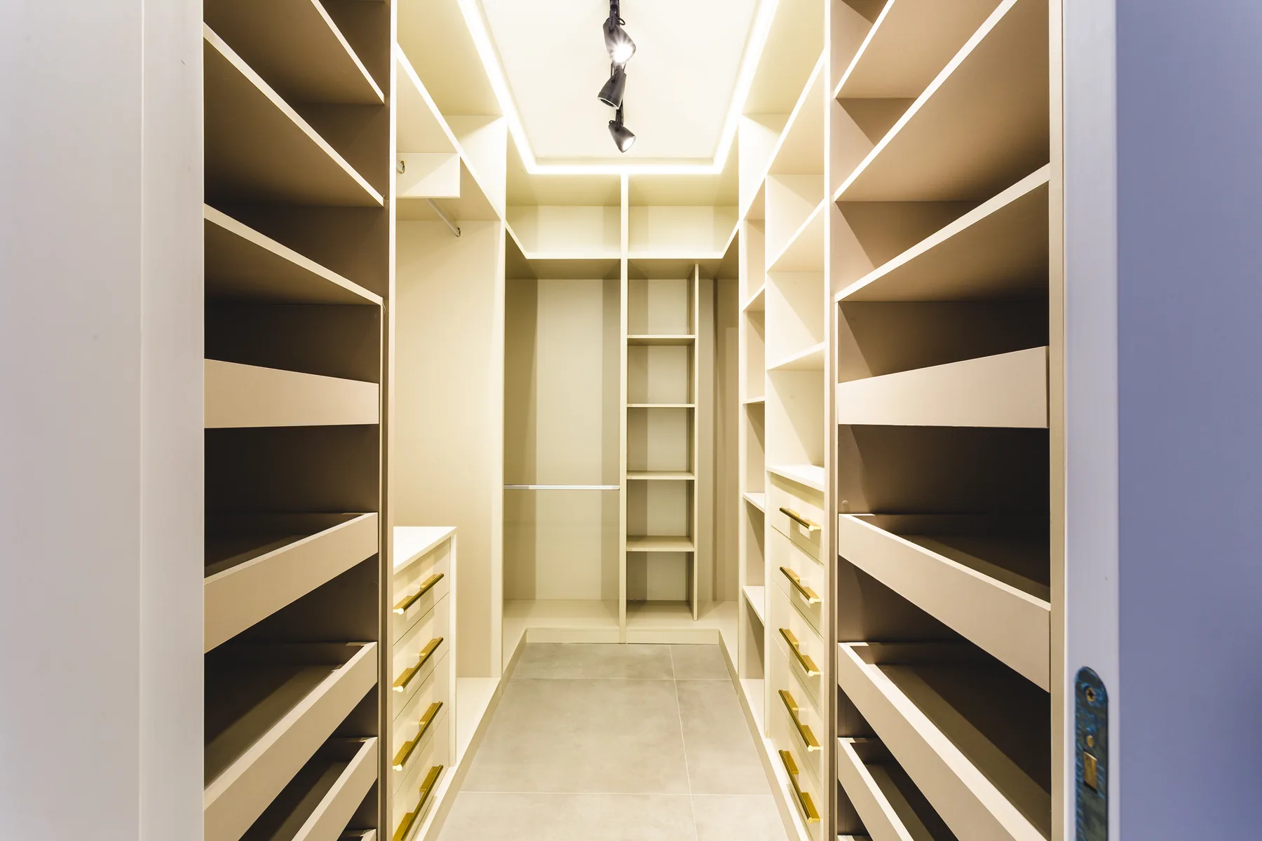 Closet planejado sob medida em U com prateleiras inclinadas para sapatos, gavetas com puxador dourado e iluminação de LED em sanca, projeto executado em Atibaia