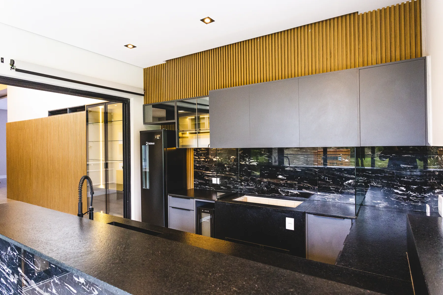 Cozinha planejada de alto padrão com bancada em mármore preto e painel ripado de madeira, projeto Casa & Design
