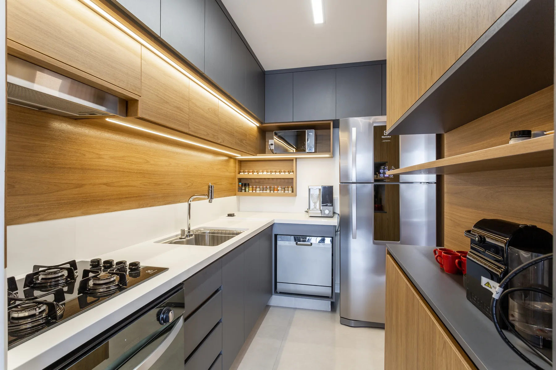 Cozinha planejada em corredor com marcenaria em madeira e cinza, cooktop embutido e bancada branca, projeto em São Paulo