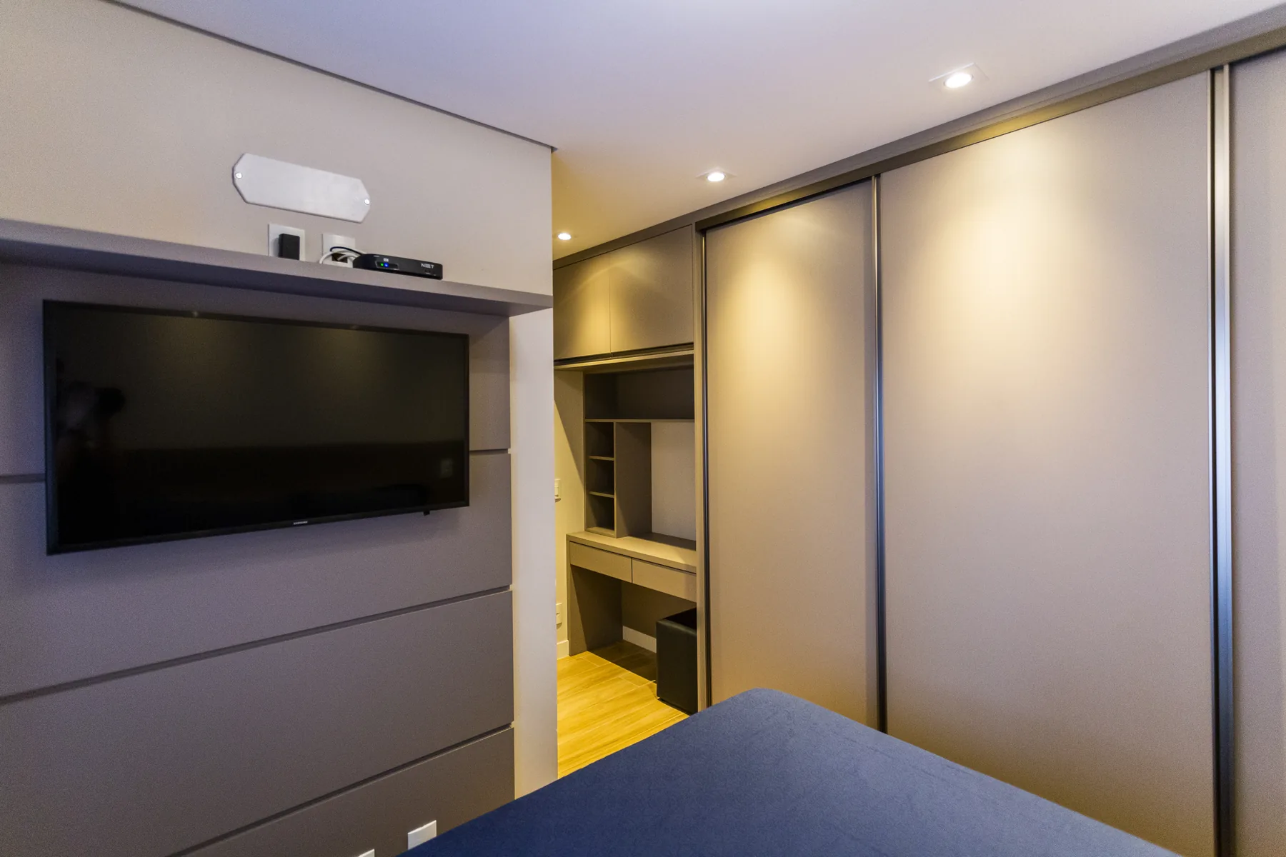 Dormitório planejado com painel de TV, guarda-roupa de correr e passagem integrada para o closet e a suíte, projeto em São Paulo
