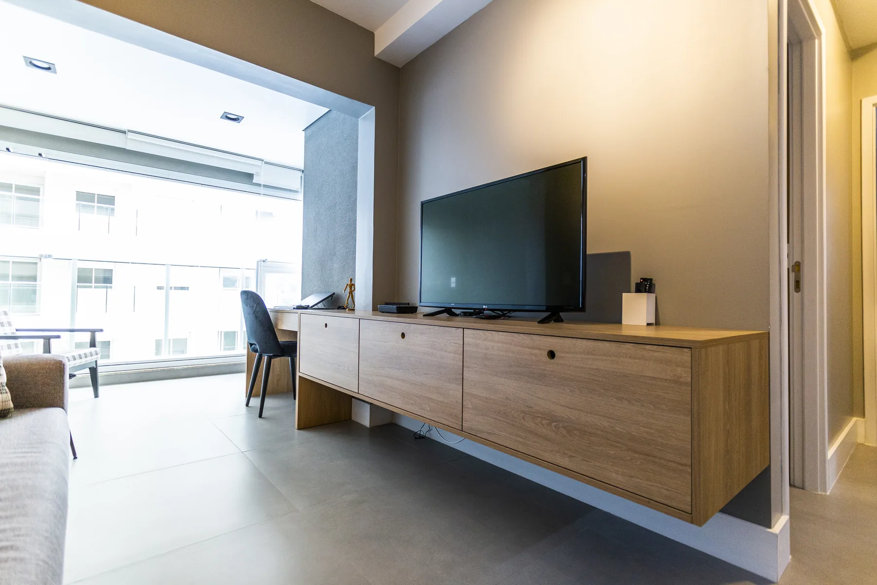 Sala de apartamento compacto com rack suspenso de madeira que se estende em escrivaninha, aproveitando toda a parede, em Atibaia